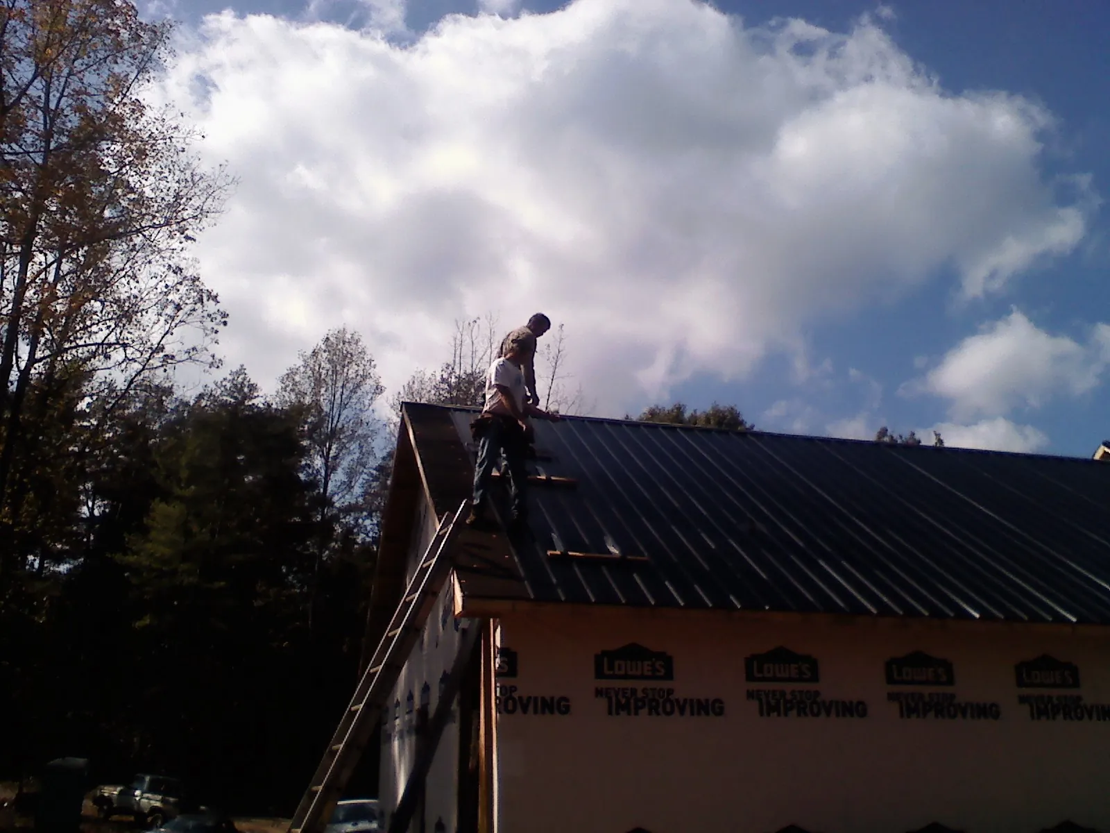 Roofer fastening dark metal panels high against a cloudy sky, from a Roof Inspection job in Brian Head